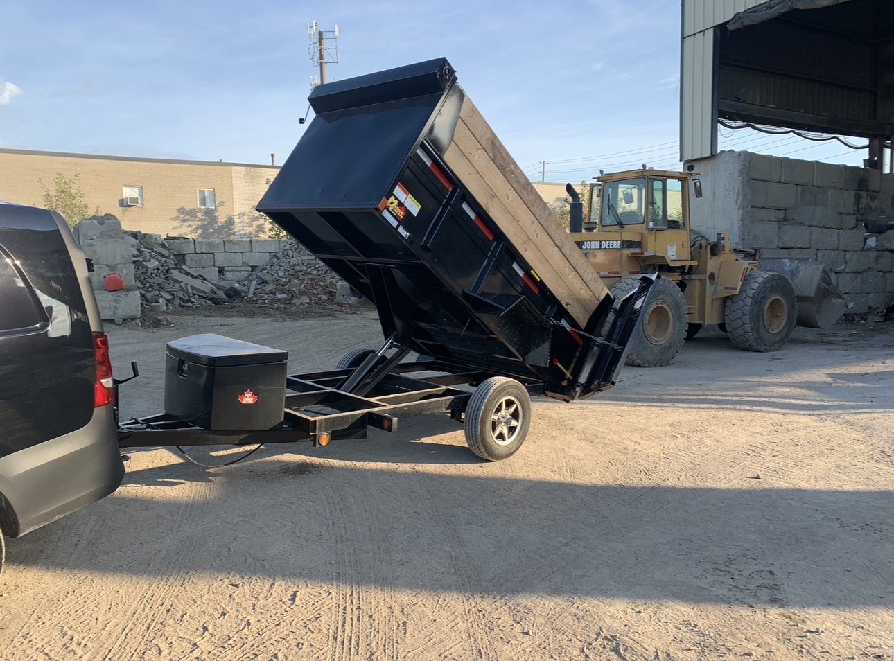 V Rentals 5x10 dump trailer with the bed raised, hitched to a tow vehicle at a Toronto yard
