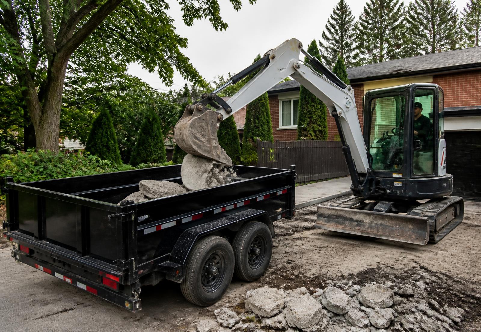 Excavator loading broken concrete into a V Rentals 5x10 dump trailer in a Toronto driveway